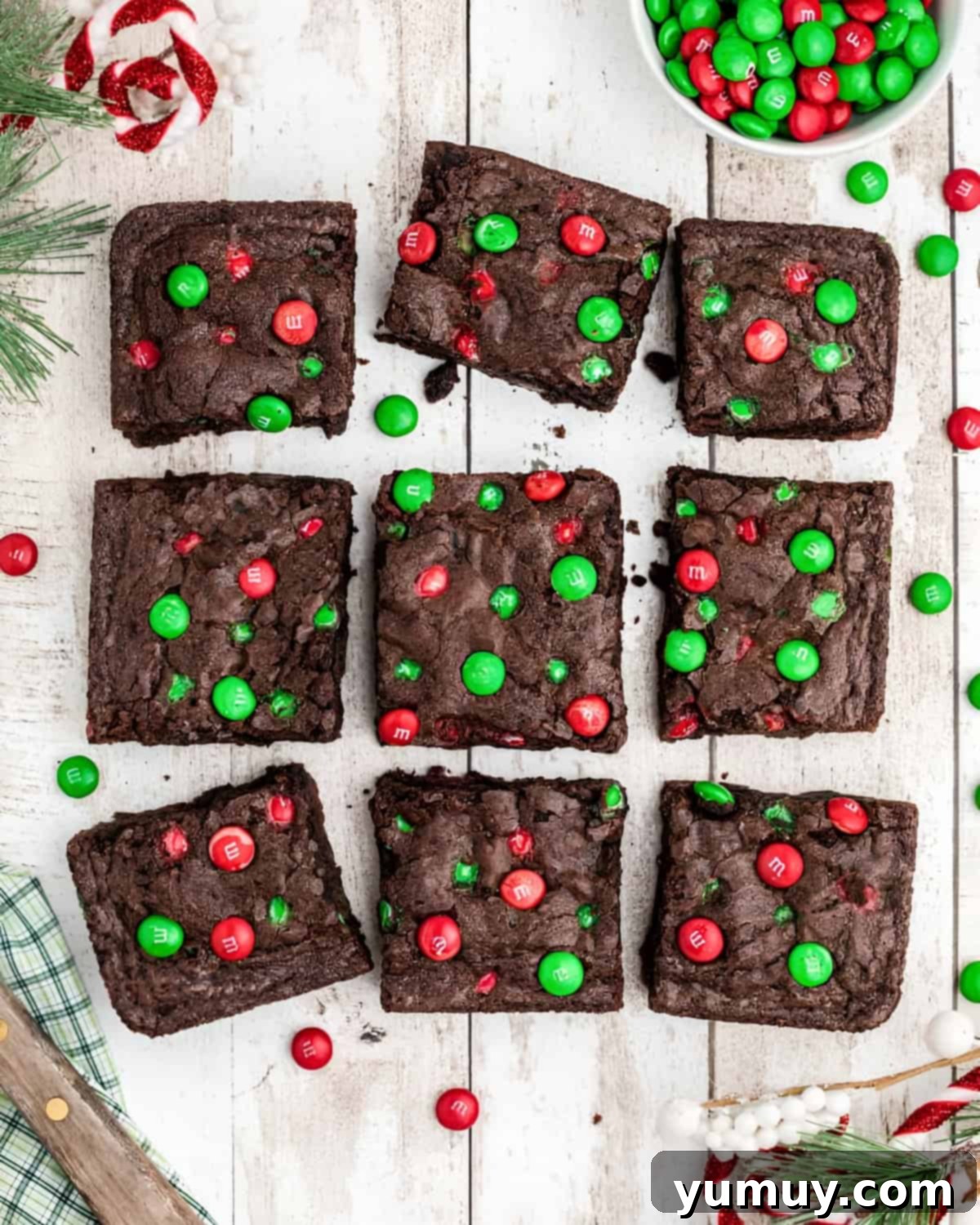 Overhead view of nine festive Christmas M&M brownies arranged on a white surface, showcasing their rich chocolate color and colorful candy toppings.