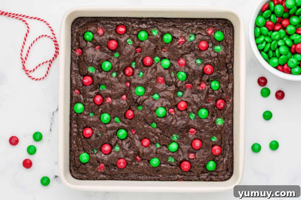 Freshly baked Christmas M&M brownies in a white baking dish, cooling on a wire rack, ready to be cut and served.