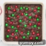 Freshly baked brownies, adorned with Christmas M&M's, resting in a white baking dish on a cooling rack.