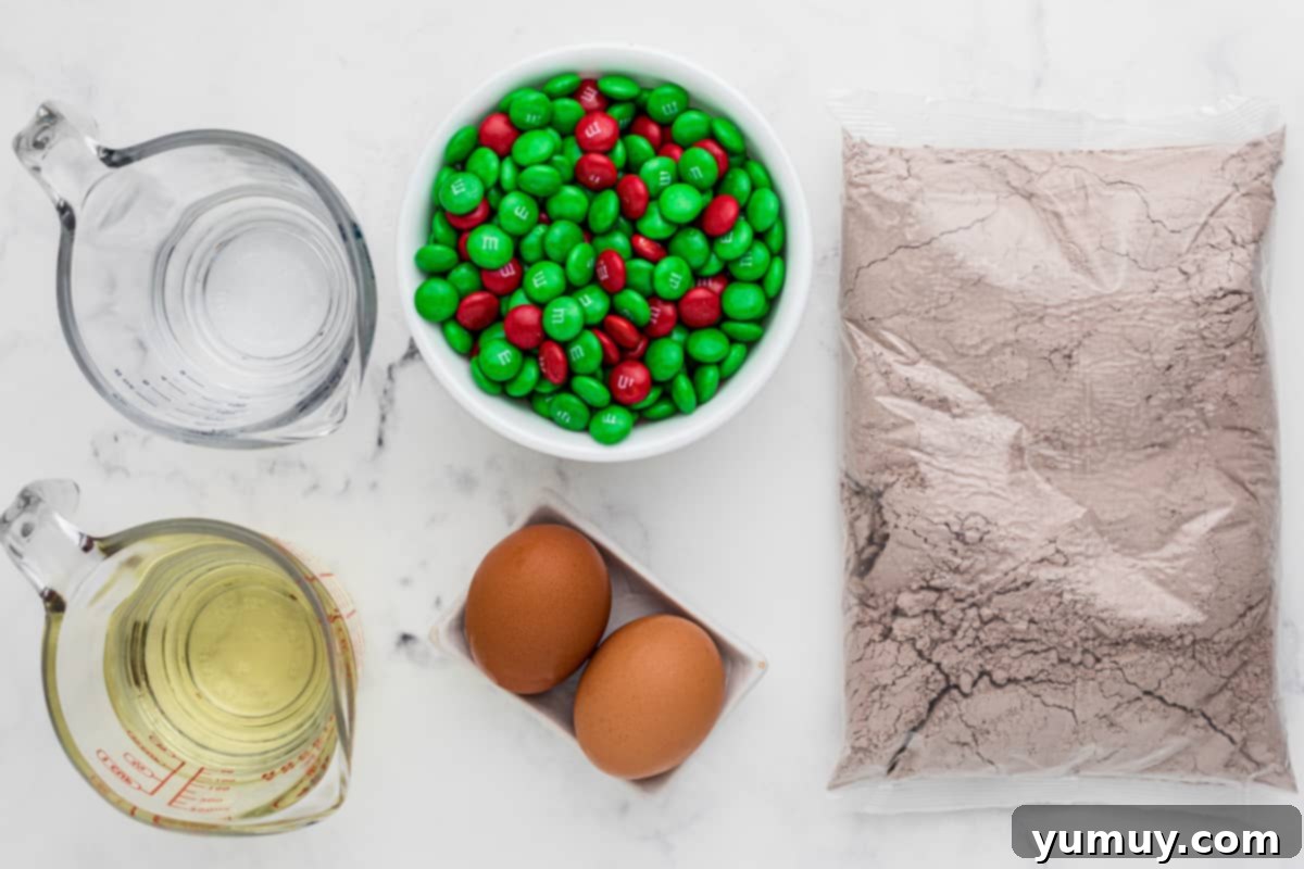 All ingredients for Christmas M&M brownies laid out: brownie mix, water, oil, egg, and colorful M&M's.