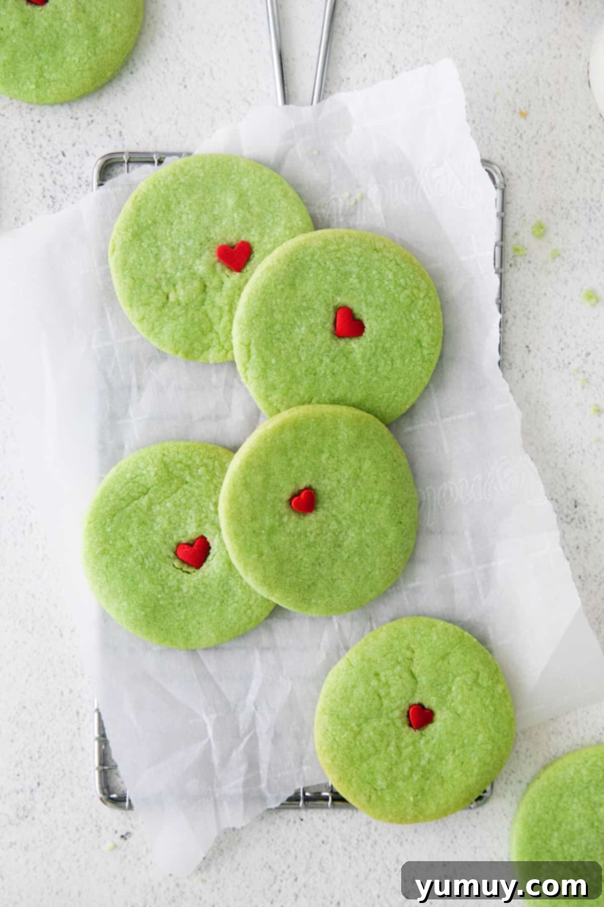 Green Grinch sugar cookies with red hearts, arranged on a tray.