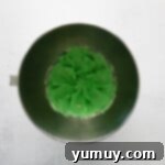 Green butter in a metal bowl on a white background.