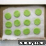 Green cookie dough circles on a baking sheet, ready for chilling.