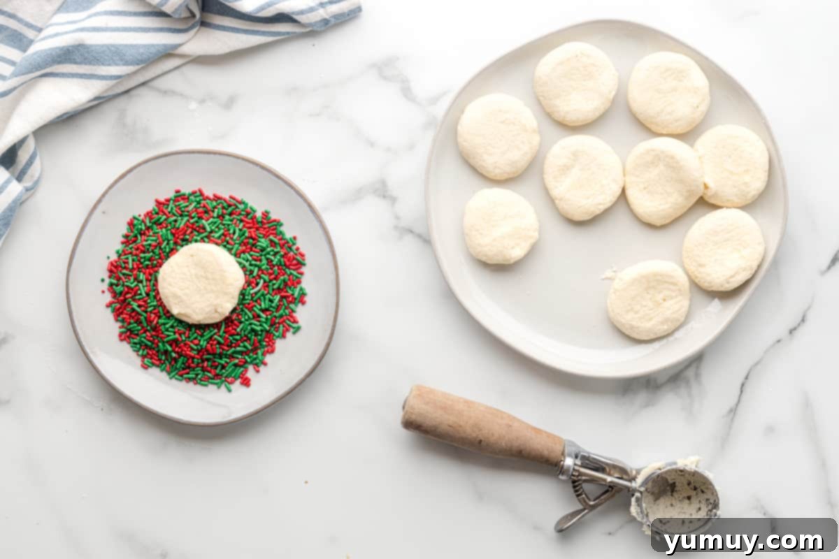 flattened sugar cookie dough balls on a white plate with one cookie dough ball in a plate of red and green sprinkles
