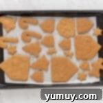 Festive Gingerbread Treats 13 Unbaked gingerbread cookies arranged on a parchment-lined baking sheet, ready for the oven.