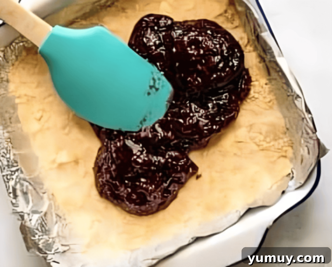 Luscious Raspberry Bars 11 A baking pan showing raspberry jam being spread evenly over a prepared shortbread crust.