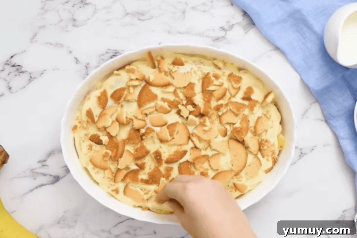 crumbling vanilla wafers over banana pudding in a baking dish.
