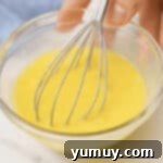 whisking raw eggs in a glass bowl.