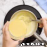 pouring tempered eggs into warm milk in a saucepan.
