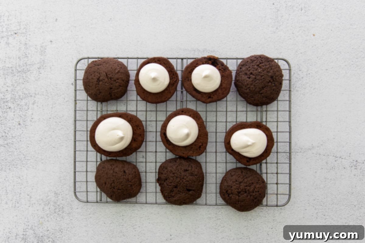 Close-up of marshmallow creme filling being expertly piped onto a chocolate whoopie pie cake on a cooling rack.