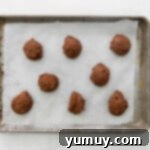 Uniform scoops of chocolate cake batter meticulously placed on a parchment-lined baking sheet.