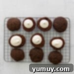 Piping the marshmallow creme filling onto one side of a chocolate whoopie pie cake on a cooling rack.