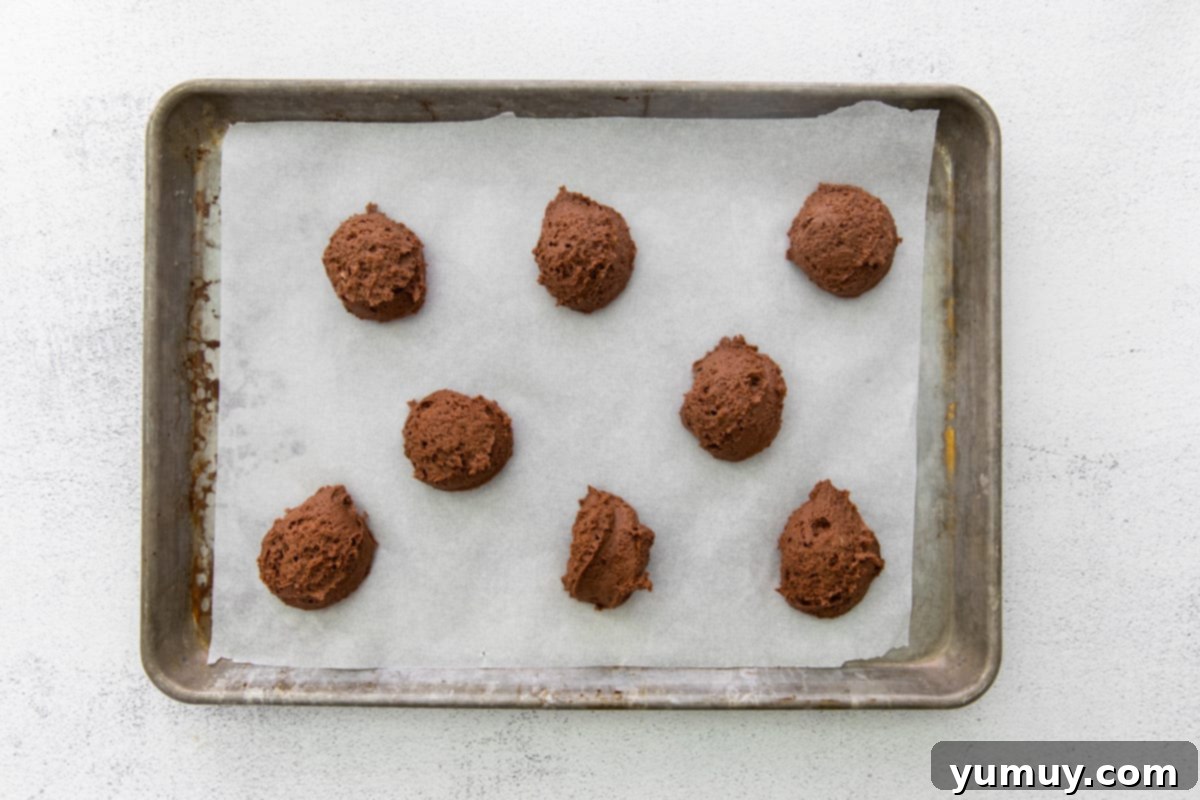 Rows of perfectly scooped chocolate cake batter on a parchment-lined baking tray, ready for the oven.