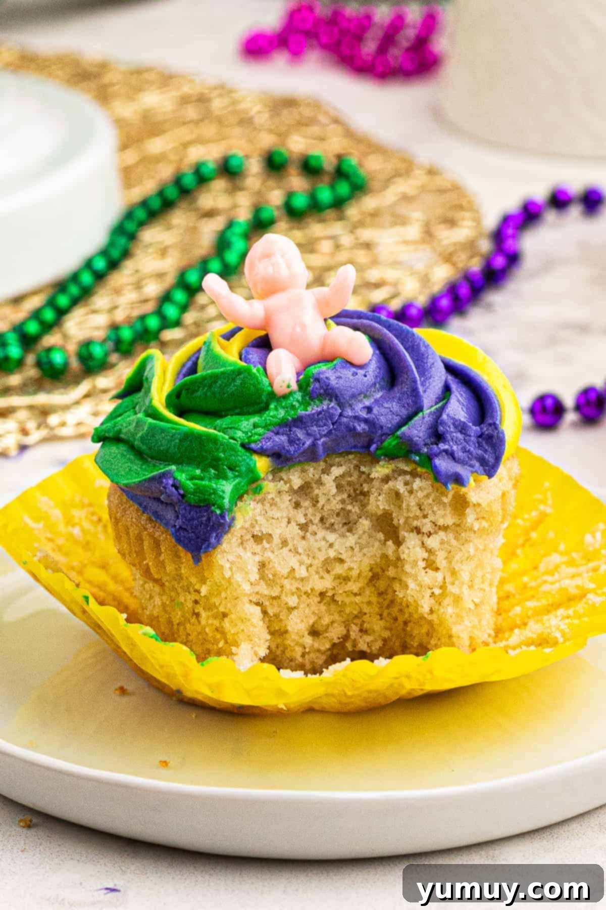 Close-up of a Mardi Gras cupcake with a bite taken out, revealing the tri-color frosting and a hidden baby.