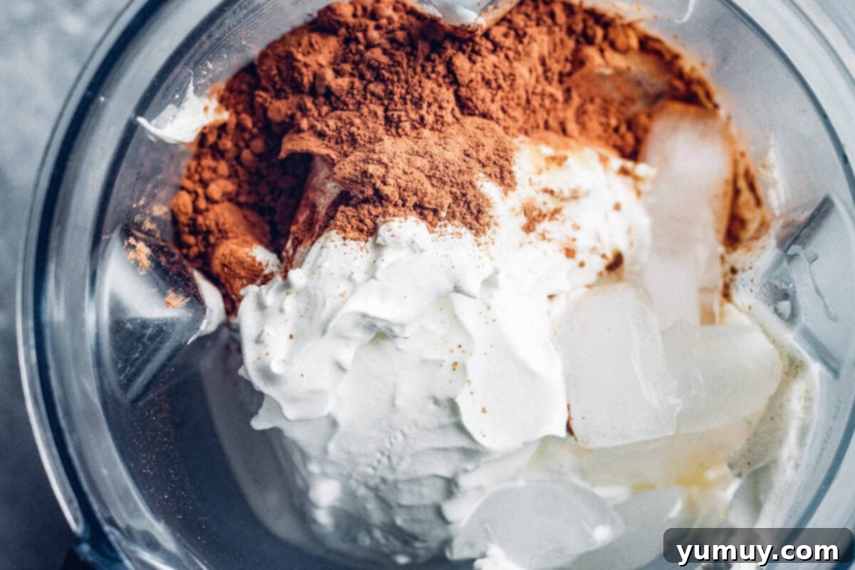 Make Your Own Wendy's Chocolate Frosty at Home 5 A blender filled with the creamy ingredients for a chocolate frosty: whipped topping, condensed milk, cocoa powder, and milk.