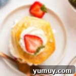 An overhead shot of an assembled strawberry shortcake, with golden biscuits, bright red strawberries, and creamy white whipped cream.