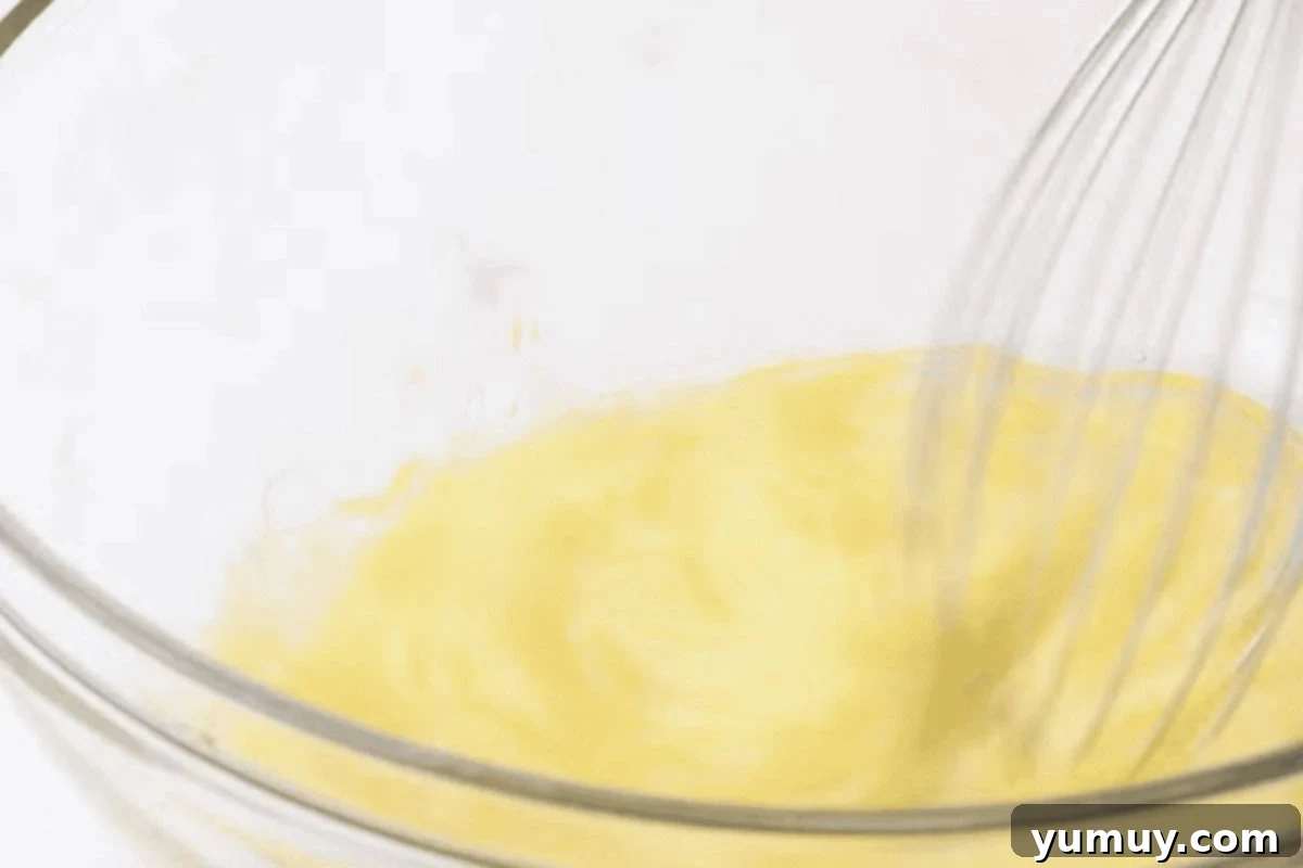 Whisking eggs and oil together in a glass bowl to create the wet base for the carrot cake layer.