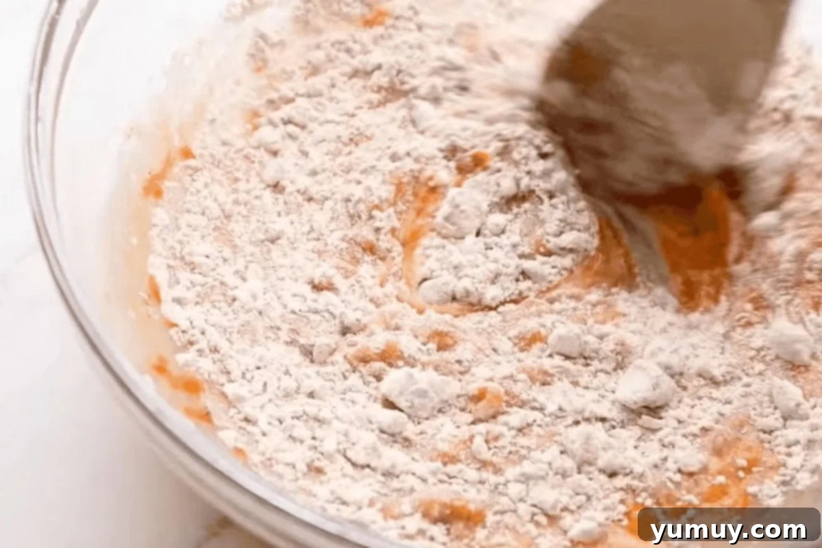 Stirring spiced flour into the mixture of carrots and eggs in a glass bowl, creating a rich carrot cake batter.