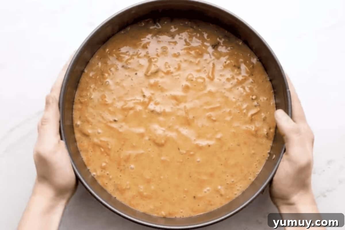 Carrot cake batter carefully poured into a springform pan, forming the base layer for the cheesecake.