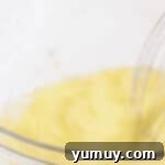 Whisking eggs and oil together in a glass bowl to create the wet base for the carrot cake layer.