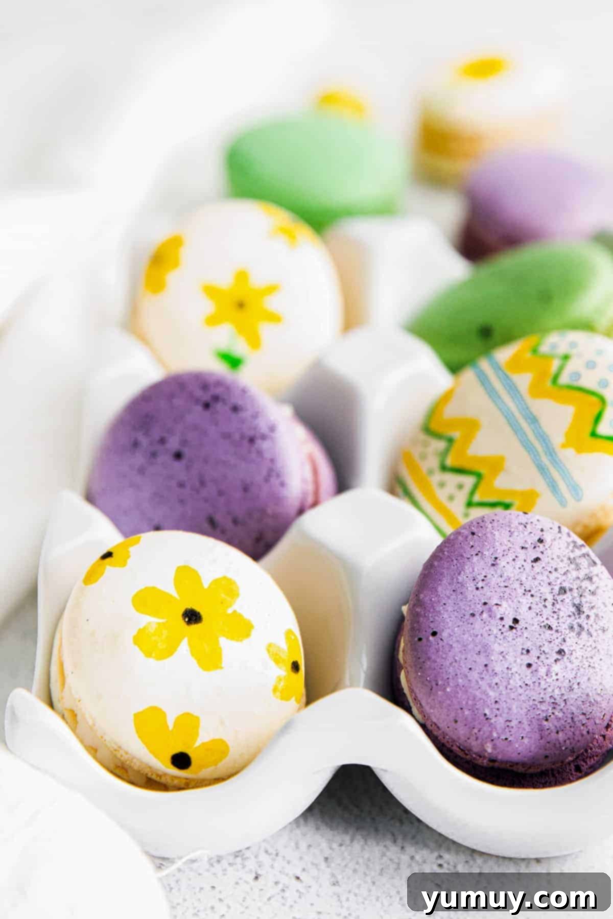 A close-up view of beautifully painted Easter egg macarons nestled in an egg crate, showcasing their delicate artistry.