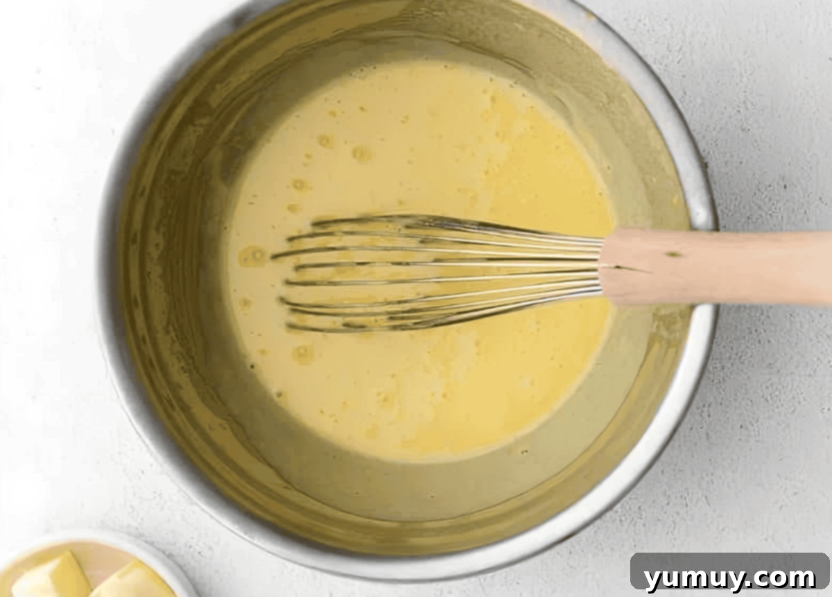 Homemade Lemon Curd: Bright, Tangy Perfection 9 Actively whisking lemon curd mixture in a heatproof bowl over a simmering saucepan.