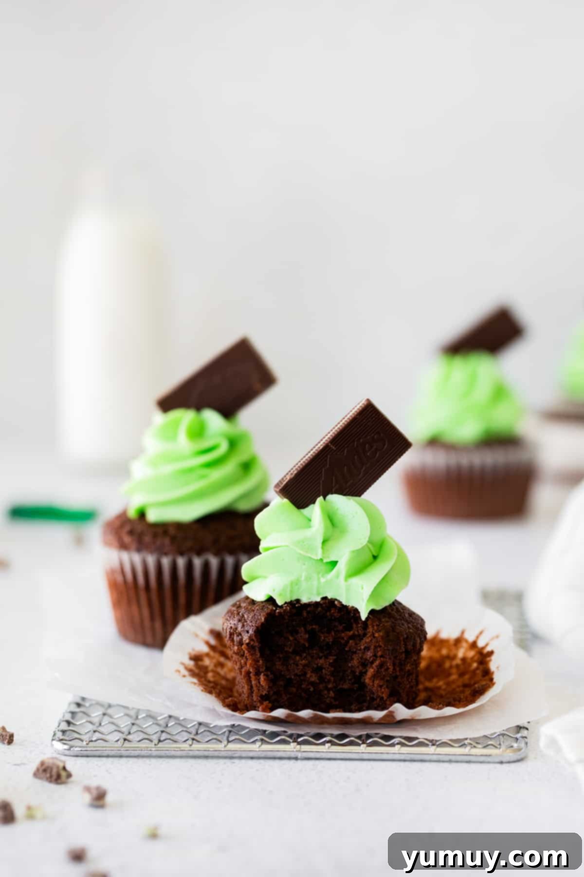 Mint Chocolate Peak Cupcakes 3 Andes mint cupcakes topped with green mint buttercream frosting and Andes chocolates, with a bite taken out of one cupcake