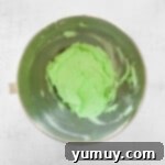 Mint Chocolate Peak Cupcakes 7 Green mint buttercream frosting in a metal bowl, showcasing its smooth and vibrant texture