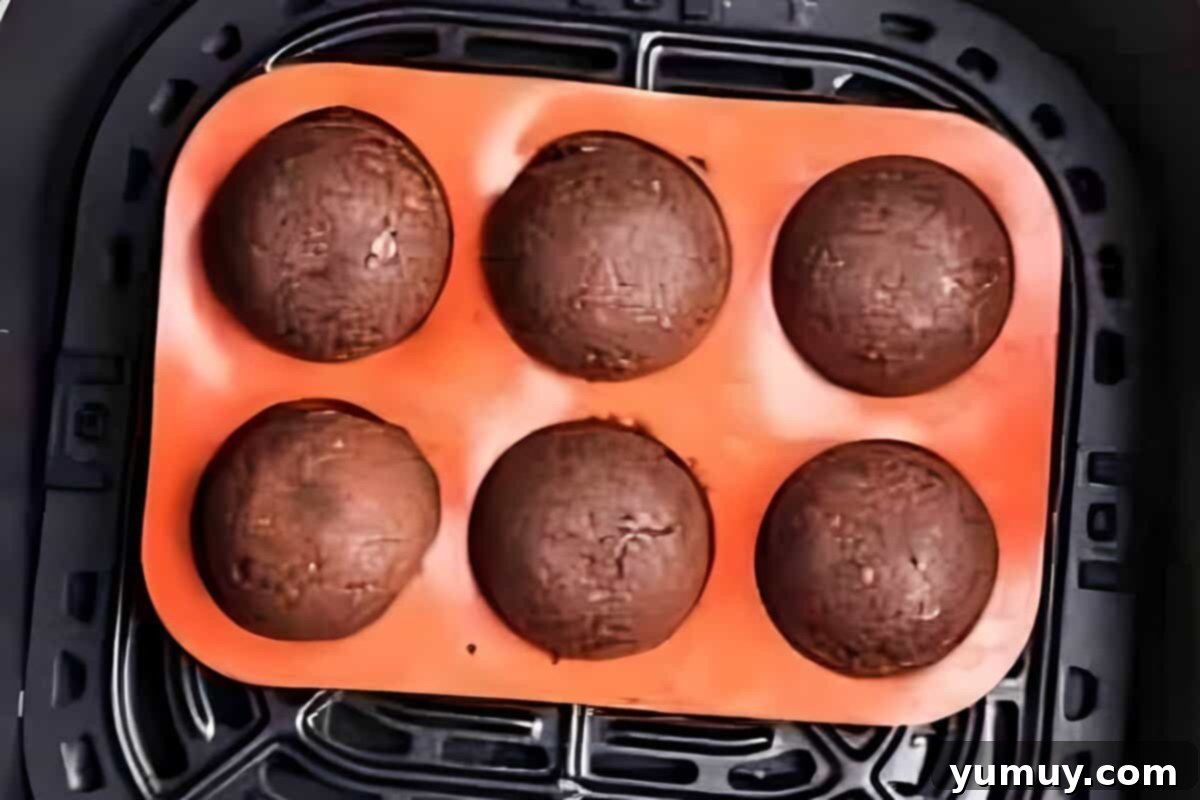 Chocolate donut holes baking in a silicone mold, inside the Air Fryer basket.