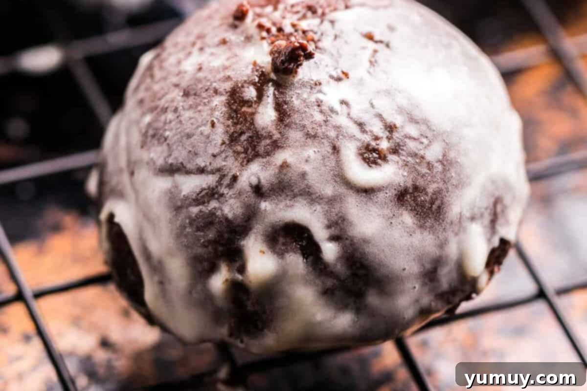 A perfectly glazed chocolate donut hole resting on a wire rack, glistening with sweet glaze.