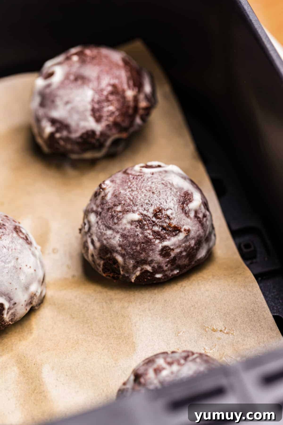 Glazed chocolate donut holes made in an air fryer on parchment paper, showcasing their perfect roundness.