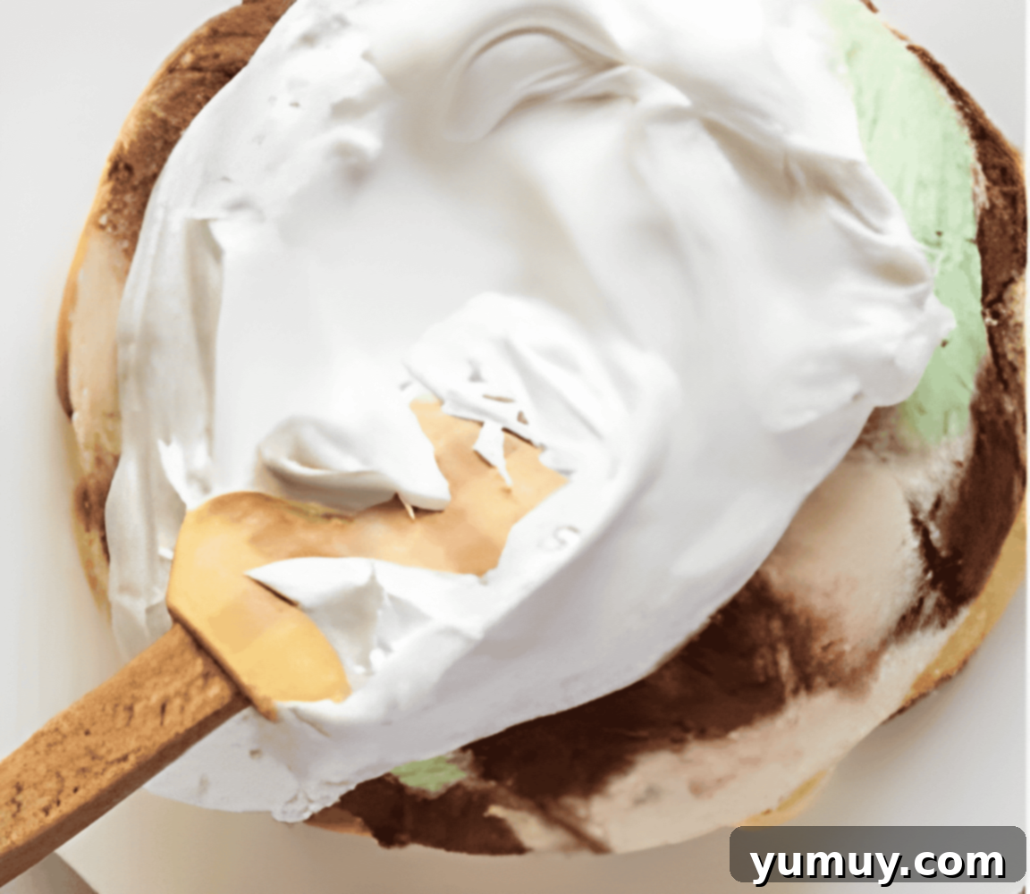 spreading meringue over an ice cream dome on a white plate.