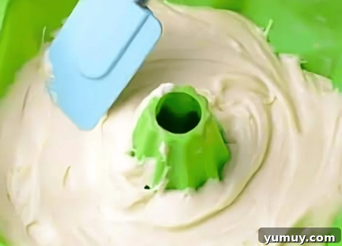 spreading batter in a green silicone bundt pan with a rubber spatula.