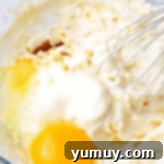 adding eggs to batter in a bowl with a whisk.