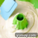spreading batter in a green silicone bundt pan with a rubber spatula.