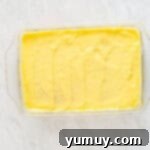 Thick pastry cream generously layered over the poked yellow cake in a glass baking dish, smoothed out and ready for chilling.