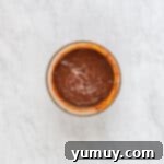 Smooth, rich chocolate ganache glistening in a clear glass bowl, freshly prepared for topping the cake.