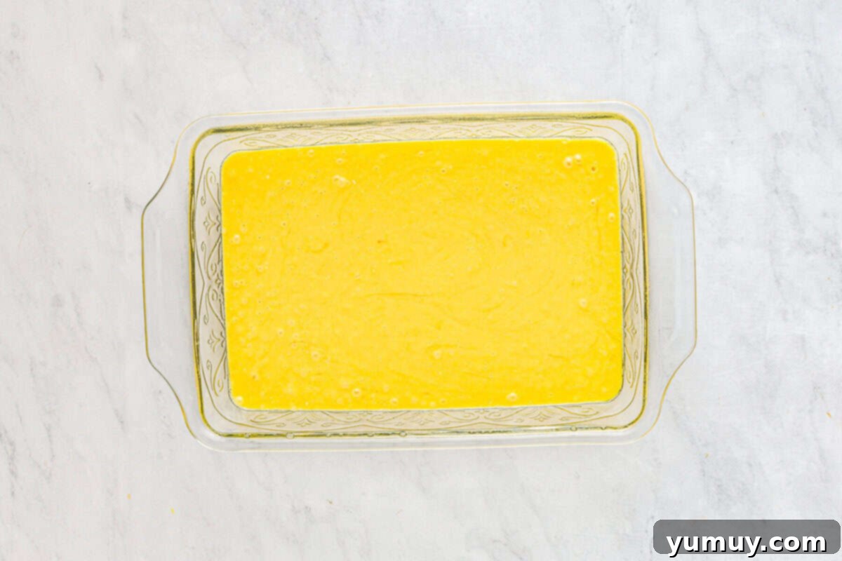 Smooth yellow cake batter evenly spread in a clear glass baking dish, ready to be baked.