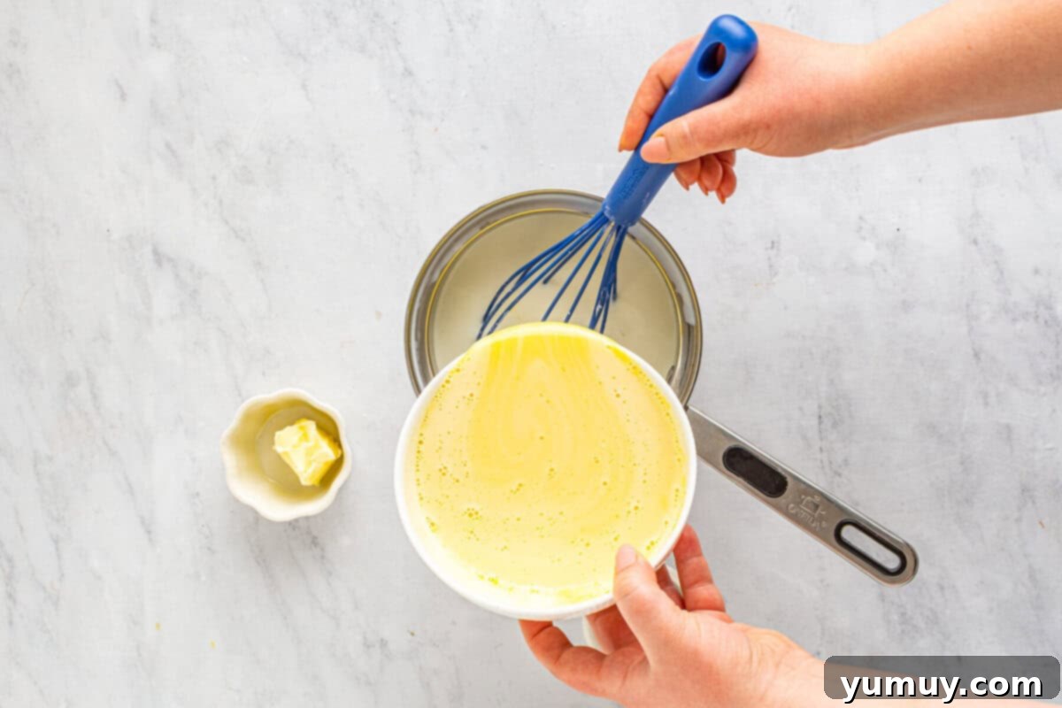 The pastry cream mixture poured back into the saucepan with the remaining milk, being vigorously whisked with a vibrant blue whisk.