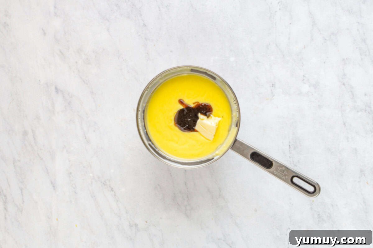 Unsalted butter and vanilla bean paste being stirred into the smooth, thickened pastry cream in a saucepan, infusing it with flavor and richness.