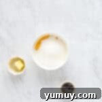 Egg yolks, granulated sugar, and cornstarch whisked until smooth and pale in a white bowl.