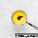 Unsalted butter and vanilla bean paste being stirred into the smooth, thickened pastry cream in a saucepan, creating a luscious texture.