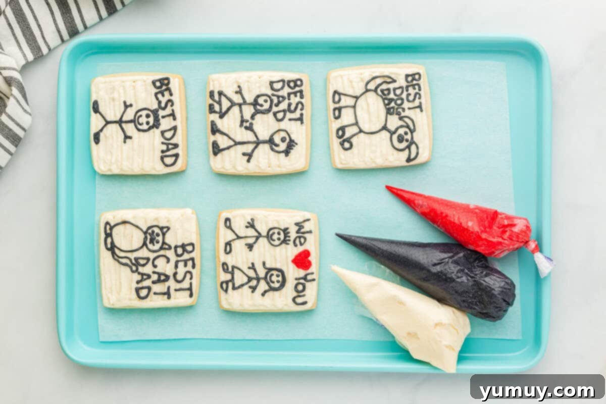 Fathers Day Cookie Creations 16 Five Father's Day cookies, adorned with red, black, and white frosting, arranged on a blue baking sheet.