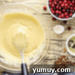 Yellow muffin batter being gently whisked in a glass bowl with a metal whisk, ready for mix-ins.