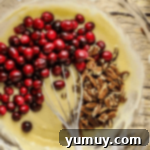 Fresh cranberries and chopped pecans being folded into the yellow muffin batter in a glass bowl.