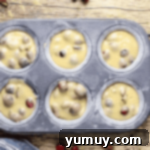 Orange cranberry pecan muffin batter neatly spooned into a muffin tin, filling each well three-quarters full.