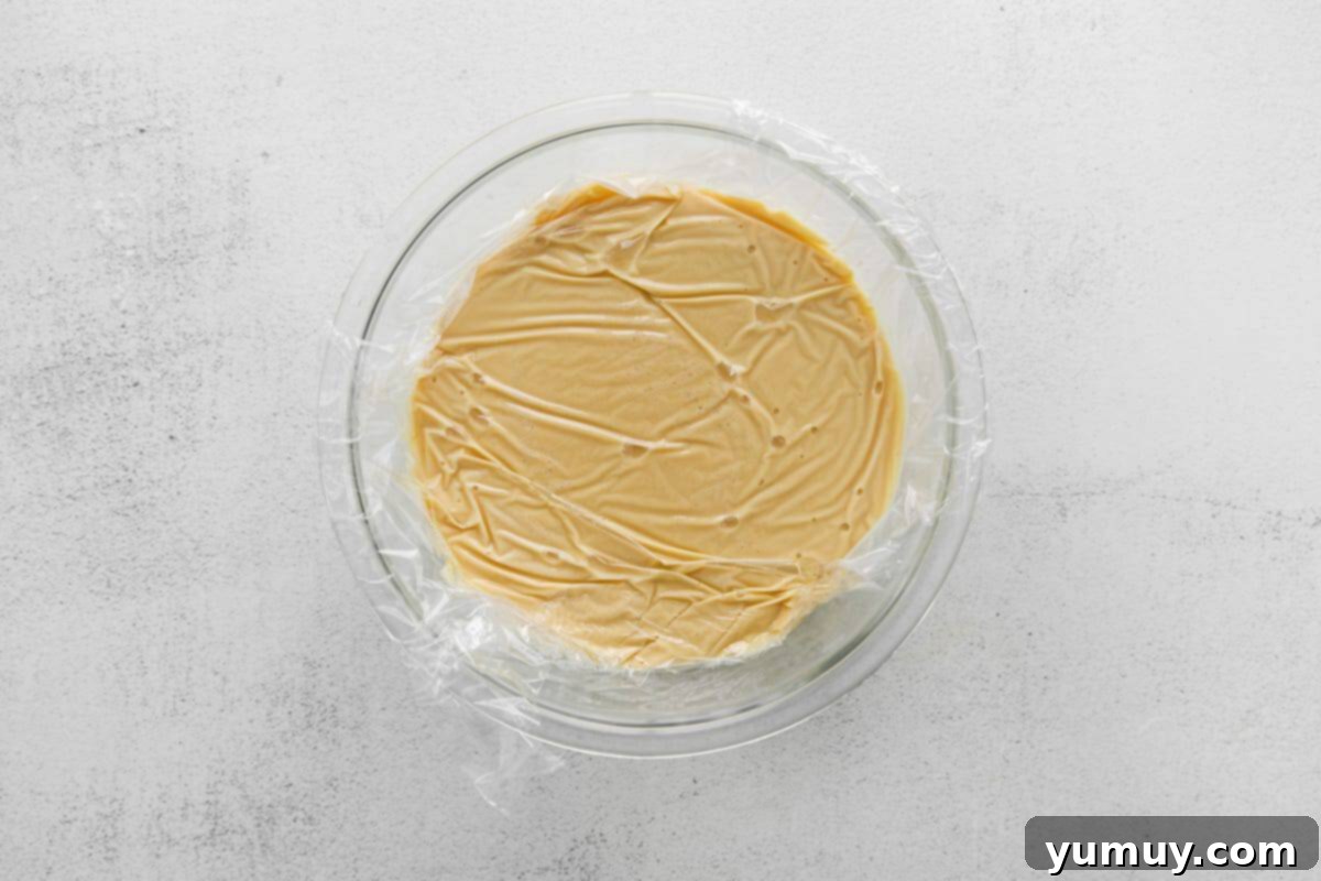 Rich Butterscotch Dream 10 budino pudding mixture in a glass bowl covered with plastic wrap.