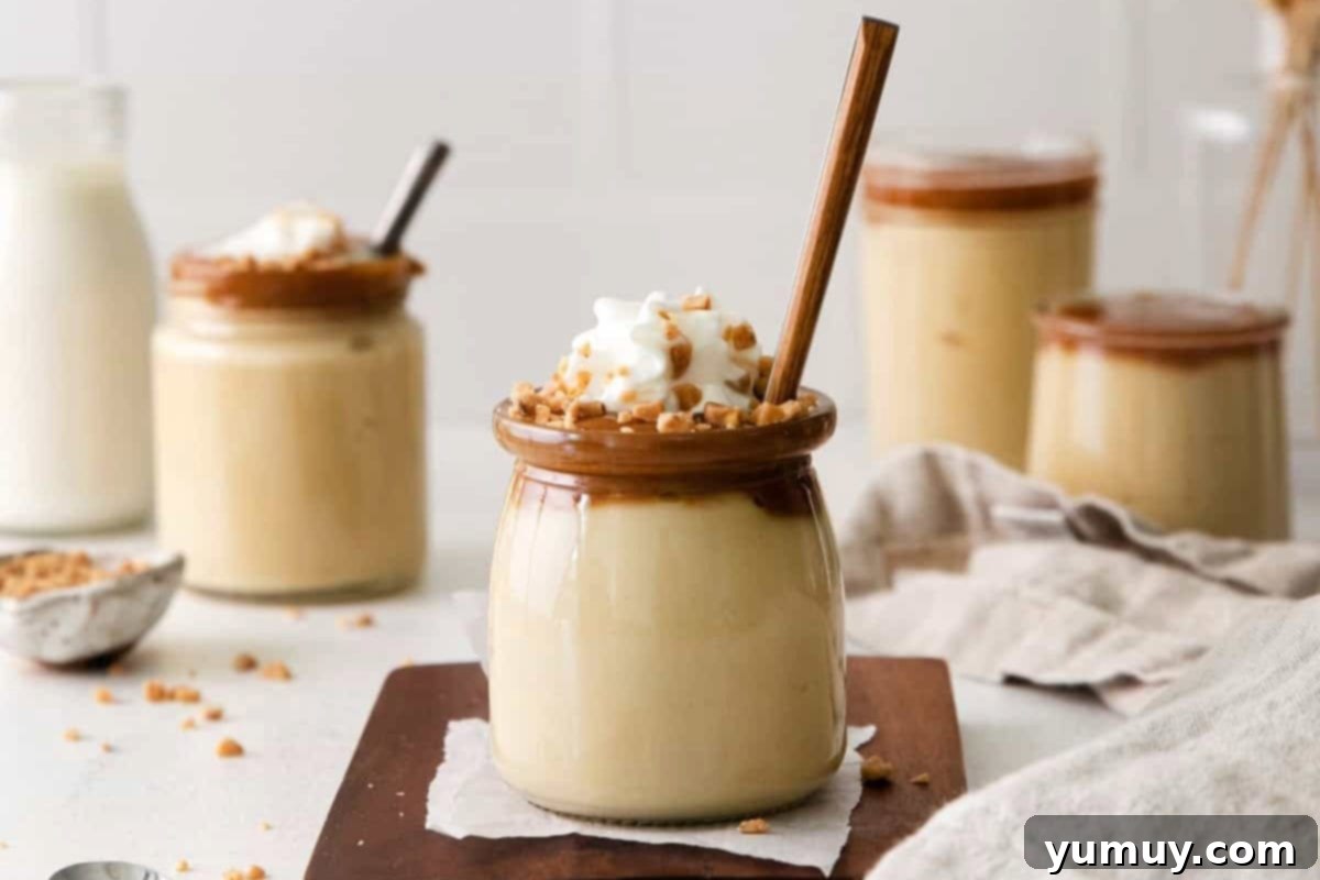 Rich Butterscotch Dream 3 butterscotch budino with a spoon on a wooden cutting board topped with whipped cream and caramel pieces.