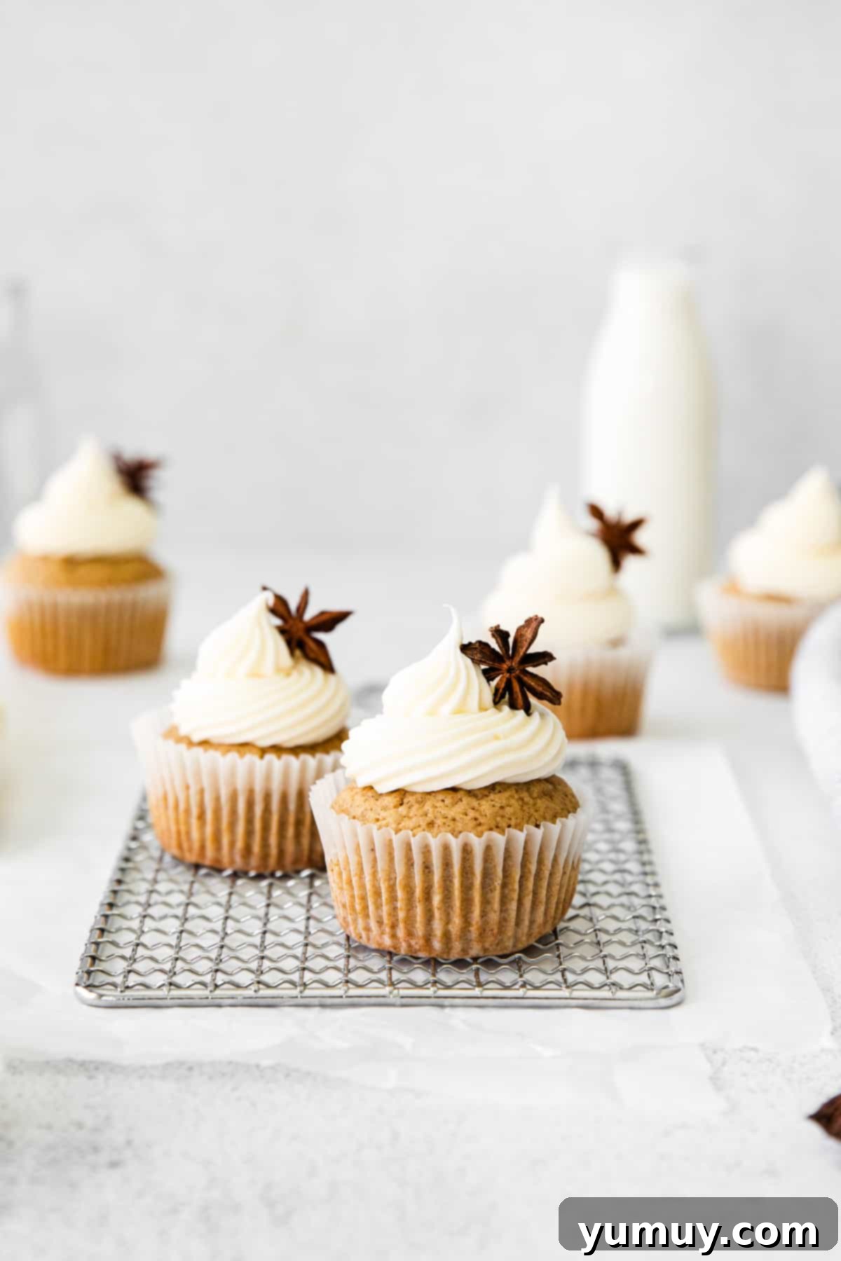 Two freshly baked chai cupcakes on a small wire rack, one featuring a decorative star anise pod.