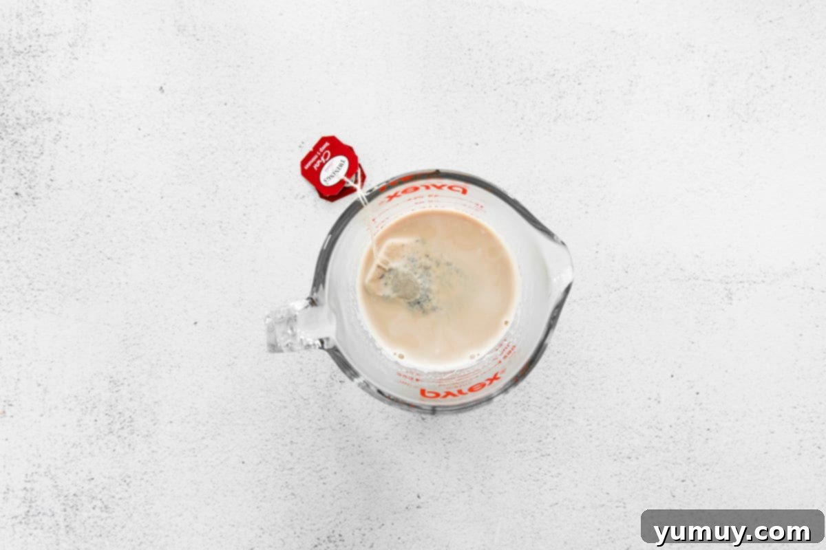 Chai tea bags steeping in warm milk in a clear glass bowl, infusing the liquid with aromatic spices.